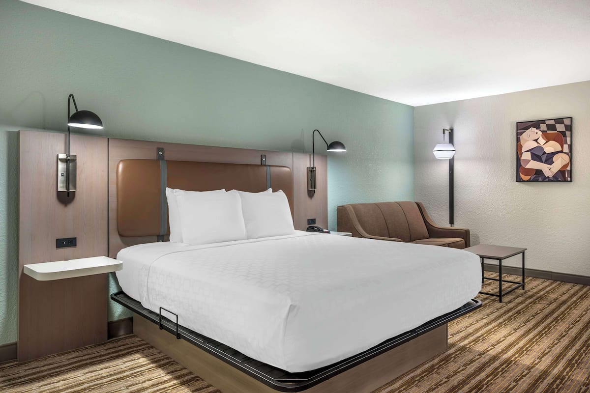 A hotel room with a large bed, bedside tables, a chair, and a lamp.