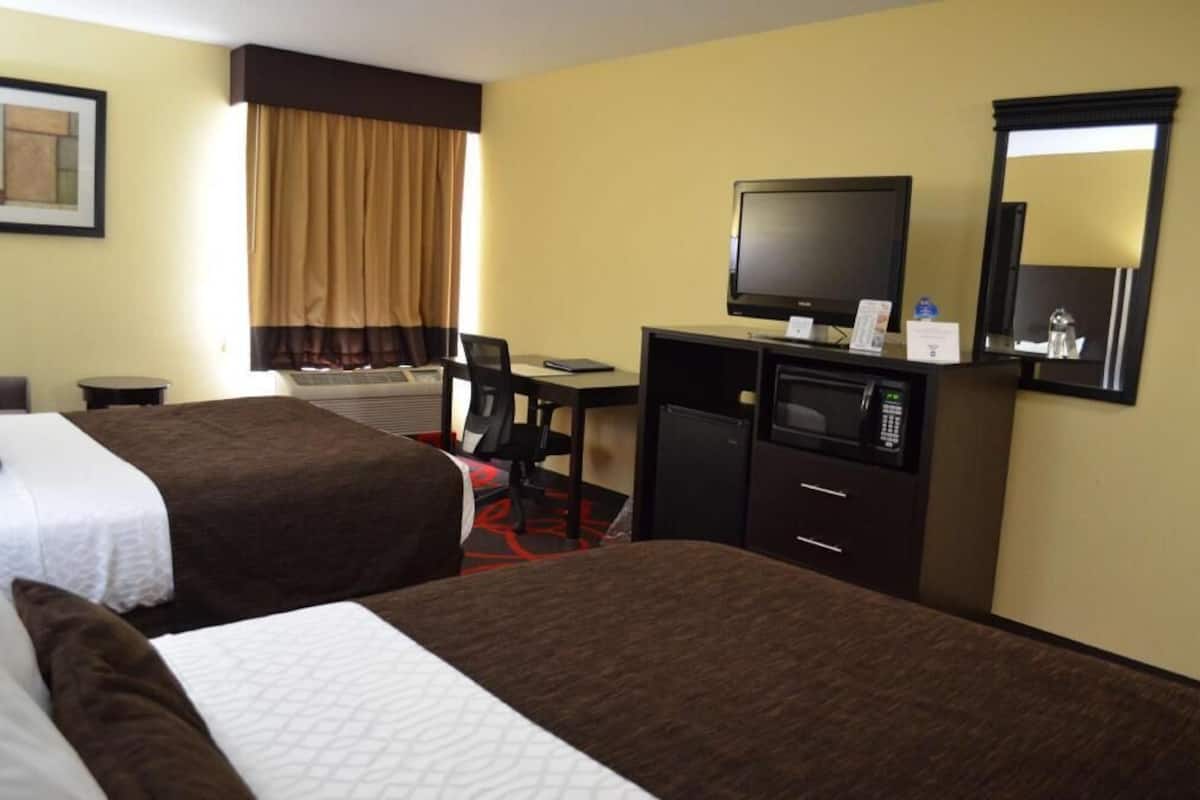 A hotel room with two beds, a desk with a computer, a television, and a mirror.