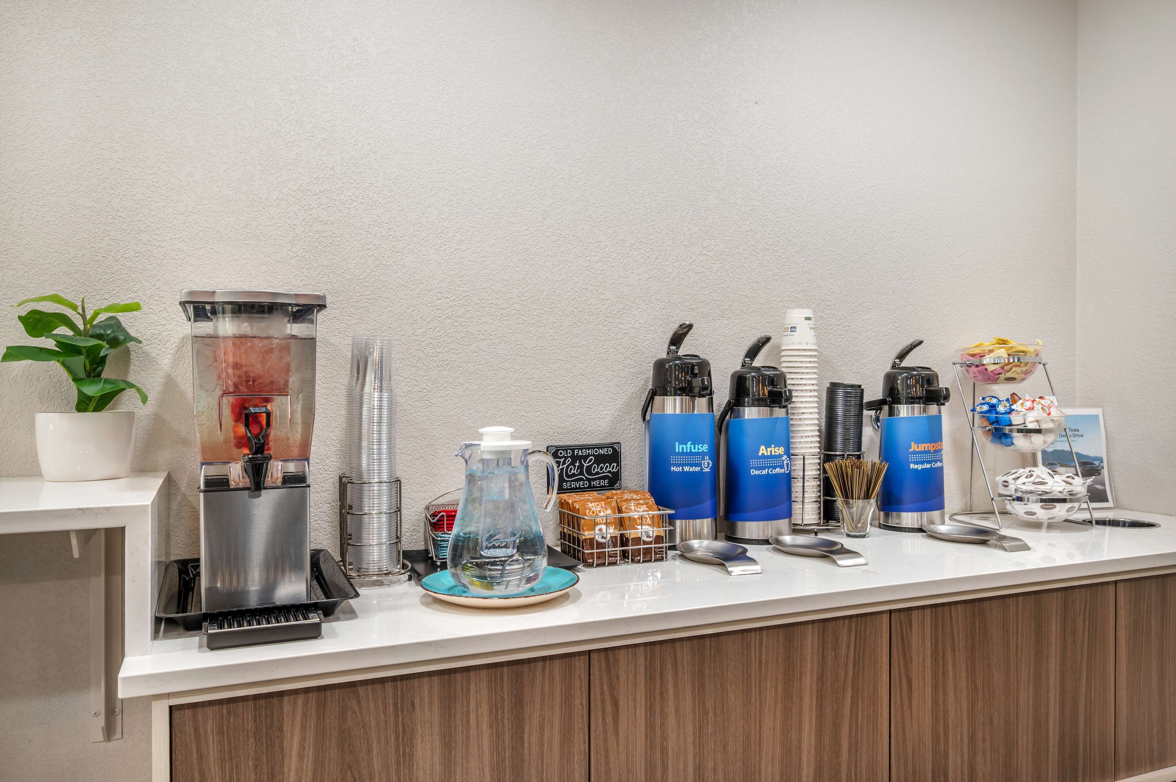 Una estación de café con varias máquinas de café, un dispensador de agua y un cartel que indica 'Old Fashioned Hot Cocoa'.