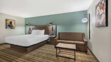 A hotel room with a large bed, a sofa, a small table, and a wall-mounted lamp.