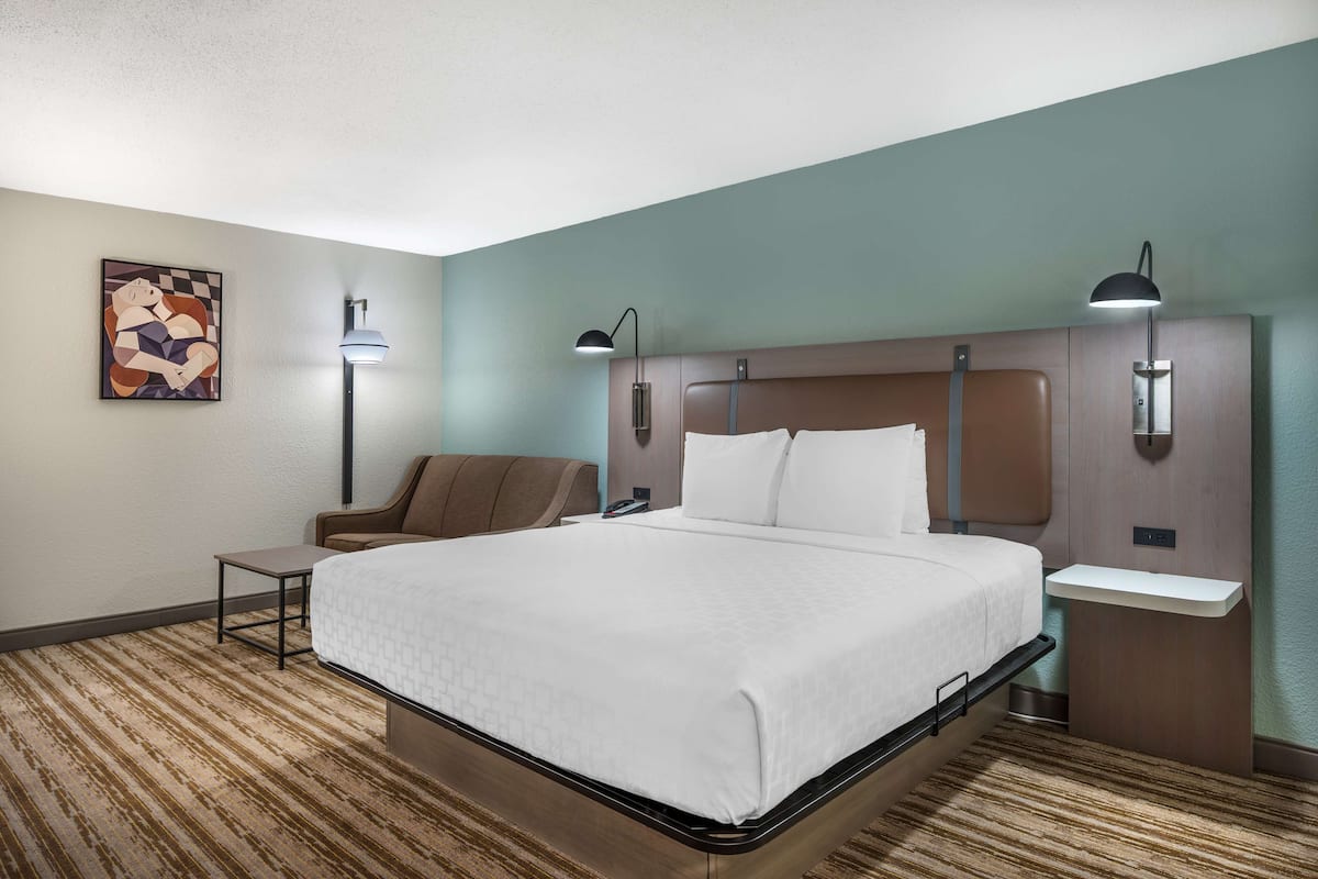 A hotel room with a bed, bedside tables, a chair, and artwork on the wall.