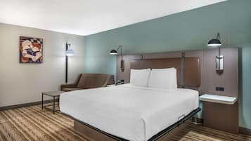 A hotel room with a bed, bedside tables, a chair, and artwork on the wall.