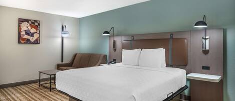 Una habitación de hotel con cama, mesitas de noche, una silla y una obra de arte en la pared.