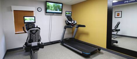 A fitness room with a treadmill, stationary bike, and a mirror.