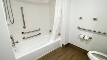 A bathroom with a white bathtub, wooden flooring, a toilet, and a shower with grab bars.