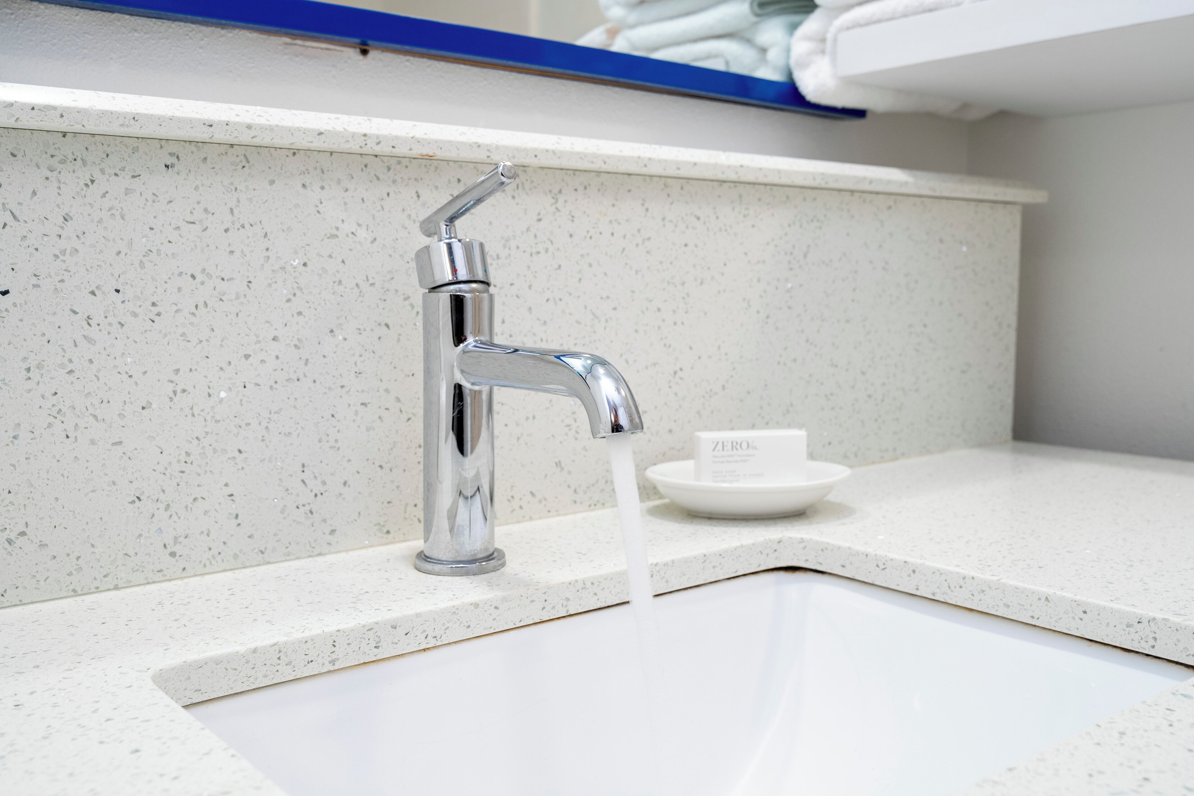 A modern bathroom with a chrome faucet, a white sink, and a soap dish.