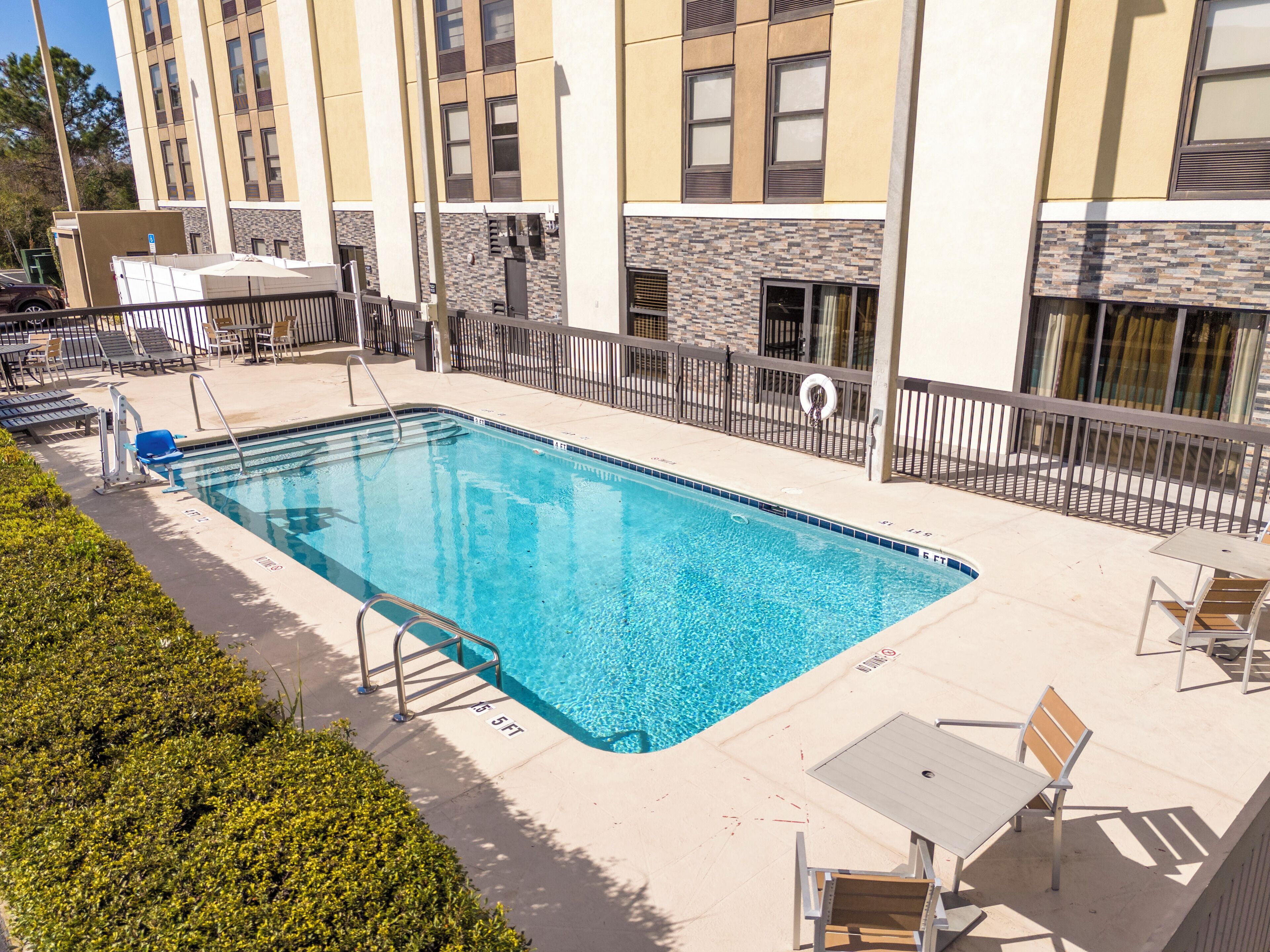 A rectangular swimming pool with a metal ladder, surrounded by a low fence and a row of lounge chairs.