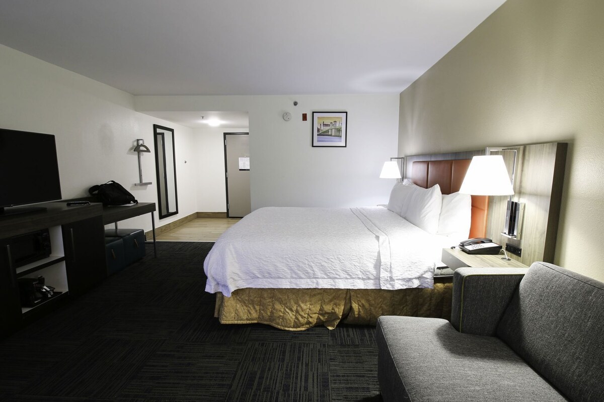 A hotel room with a bed, a desk, a TV, a lamp, and a couch.