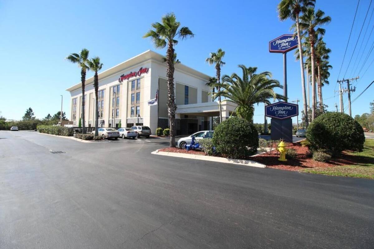 A Hampton Inn hotel with a white facade, palm trees, and a clear blue sky.