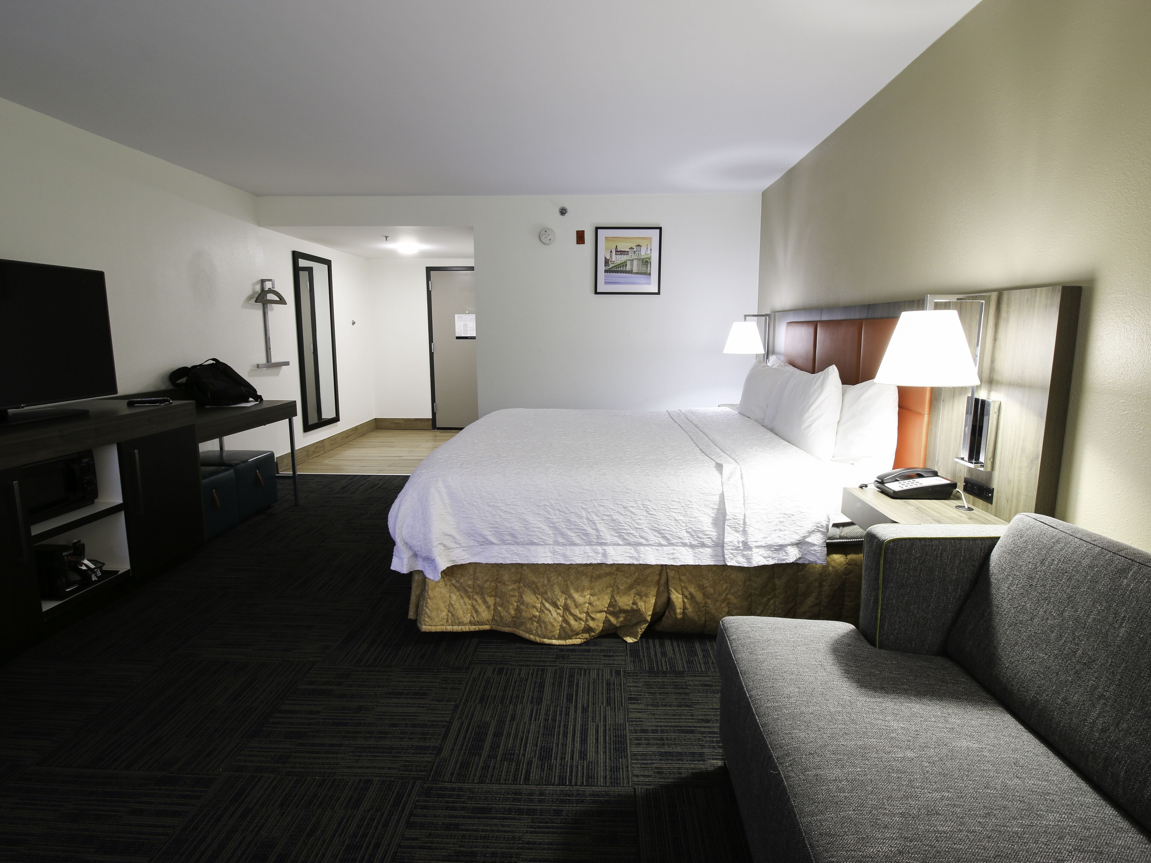 A hotel room with a bed, a desk, a television, a lamp, and a couch.
