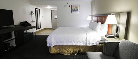 A hotel room with a bed, a desk, a television, a lamp, and a couch.