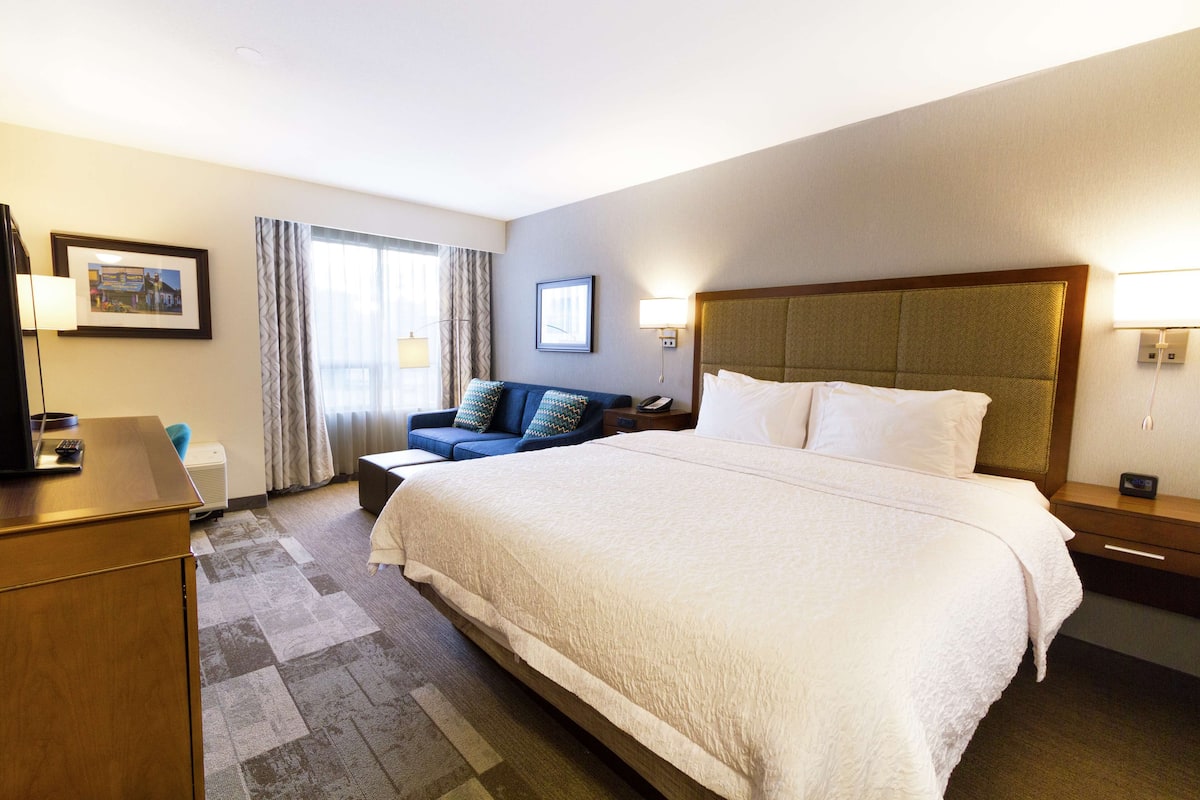 A hotel room with a large bed, a sofa, a desk, and a lamp.