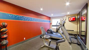 A gym with exercise equipment, a wall with a colorful design, and a television on the wall.