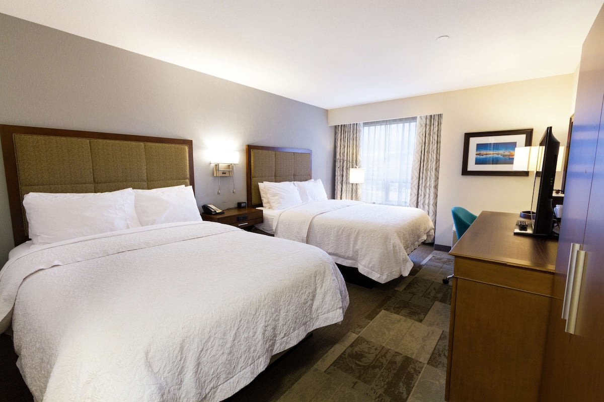 A hotel room with two beds, a desk, a chair, a TV, and a window with curtains.