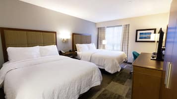 Ein Hotelzimmer mit zwei Betten, einem Schreibtisch, einem Stuhl, einem Fernseher und einem Fenster mit Vorhängen.