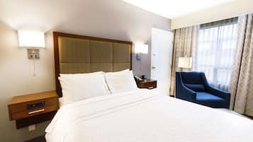 A hotel room with a large bed, a wooden nightstand, a blue armchair, and two wall-mounted lamps.