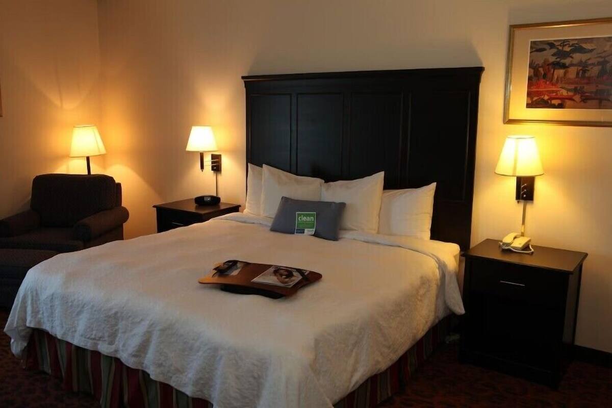 A hotel room with a large bed, two bedside tables with lamps, a chair, and a framed picture on the wall.