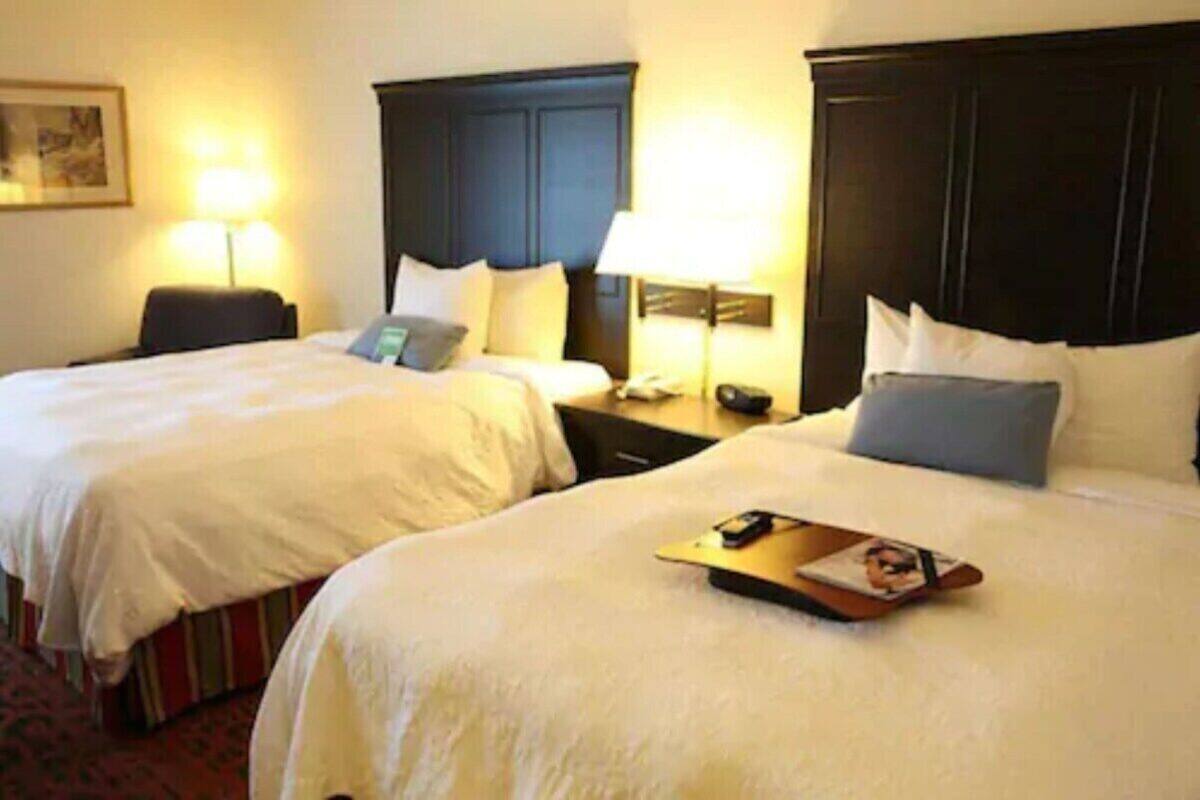A hotel room with two beds, each with a headboard, bedside tables, and lamps.