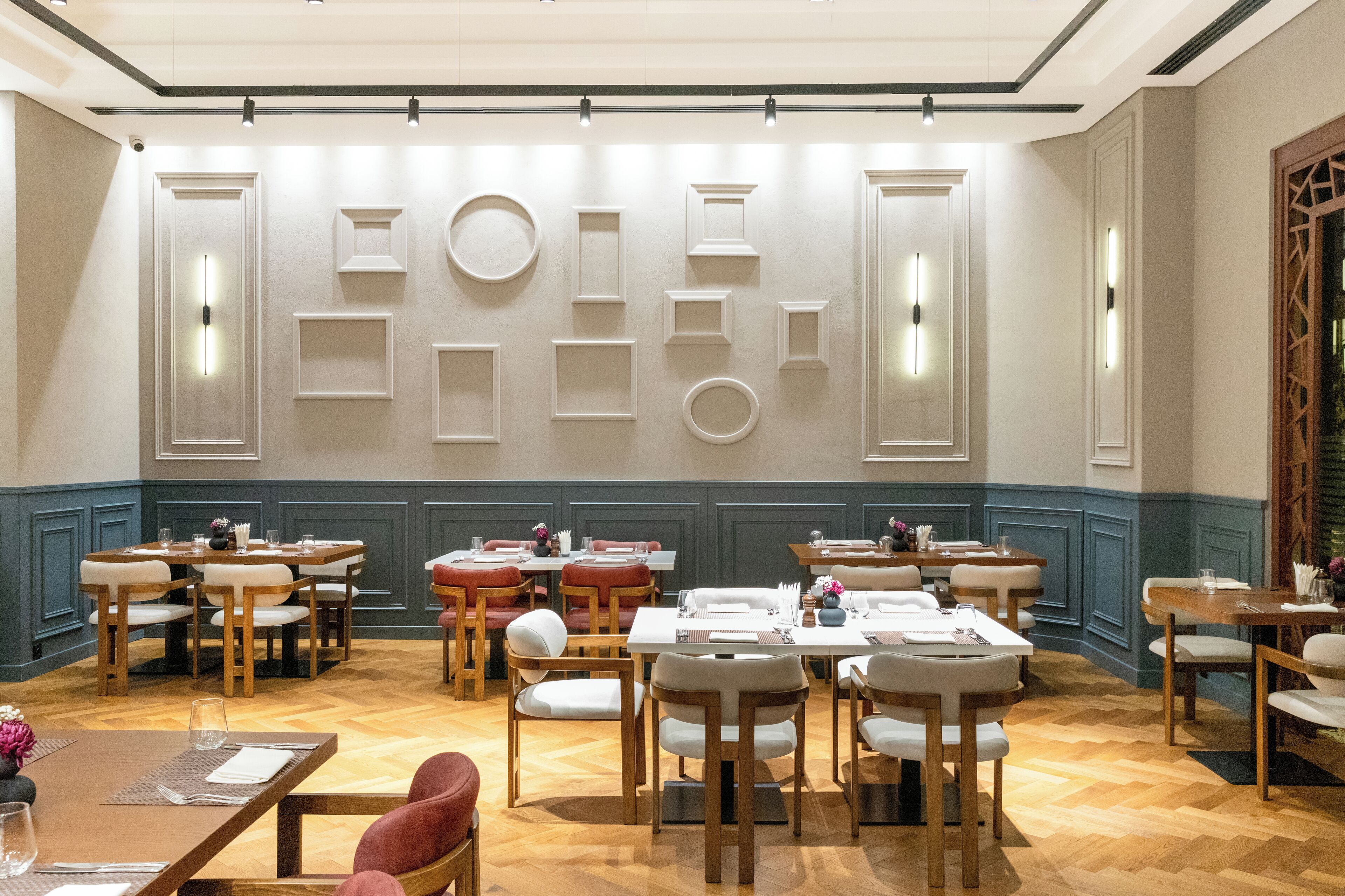 A dining area with multiple tables and chairs, a wall with geometric light fixtures, and a wooden floor.