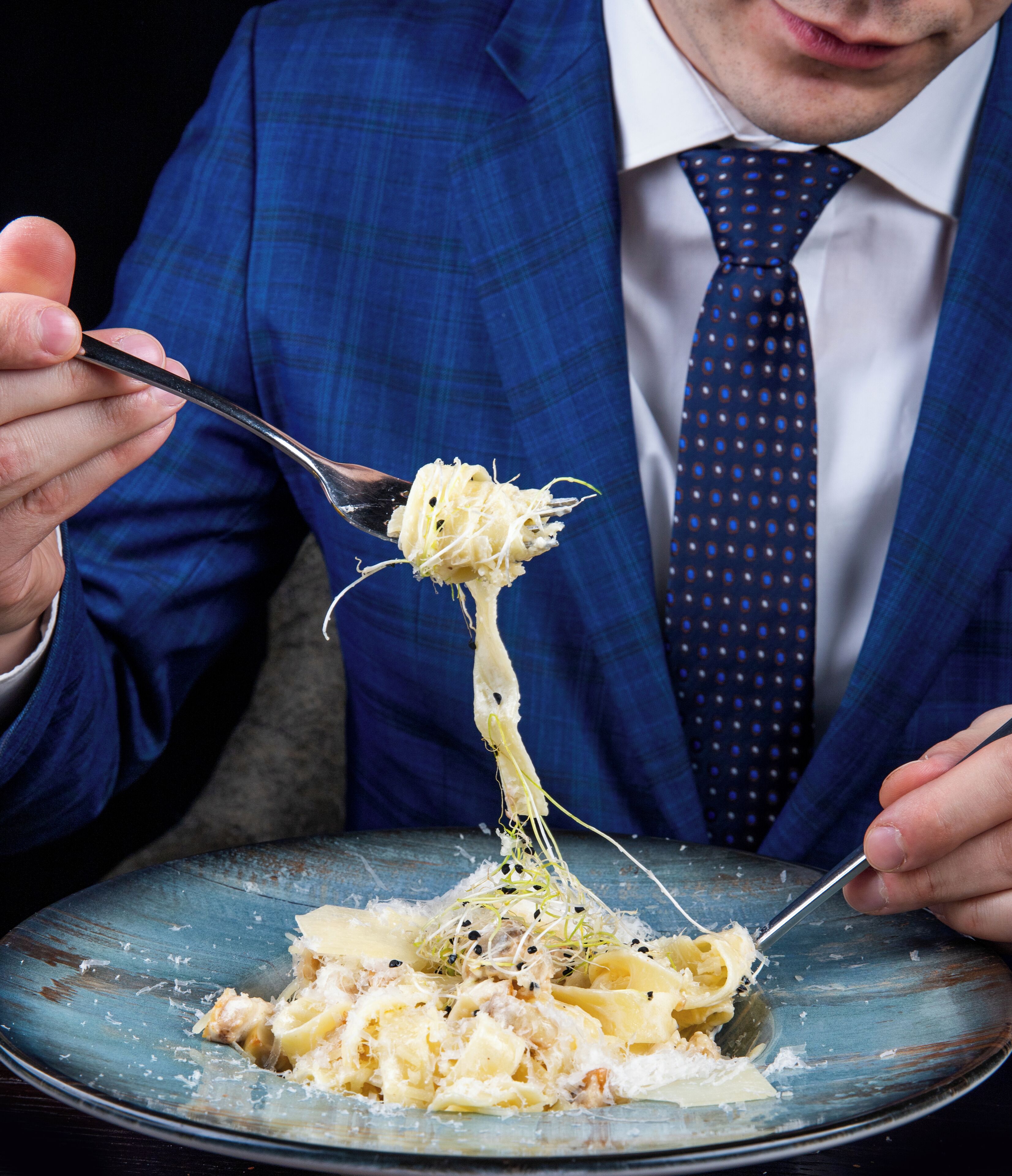 A person in a blue suit and tie holding a fork with spaghetti.