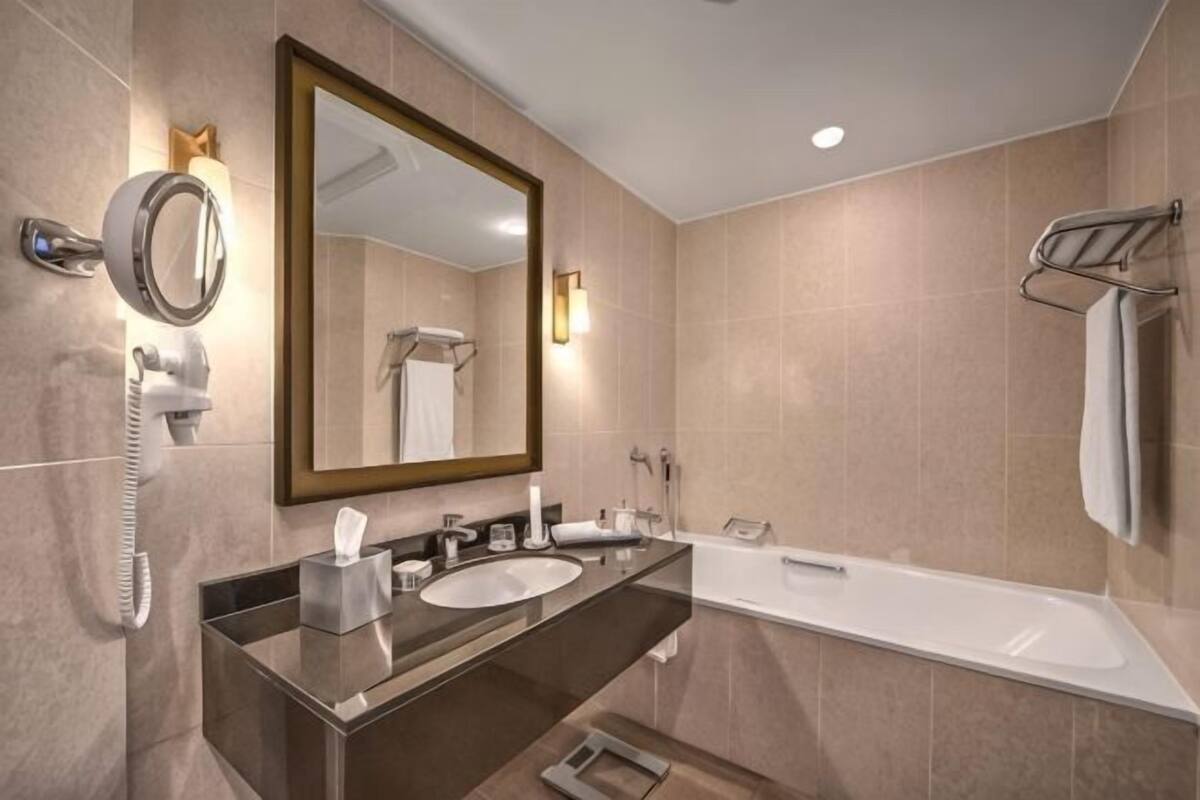 A modern bathroom with a double sink, a large mirror, a bathtub, and a towel rack.