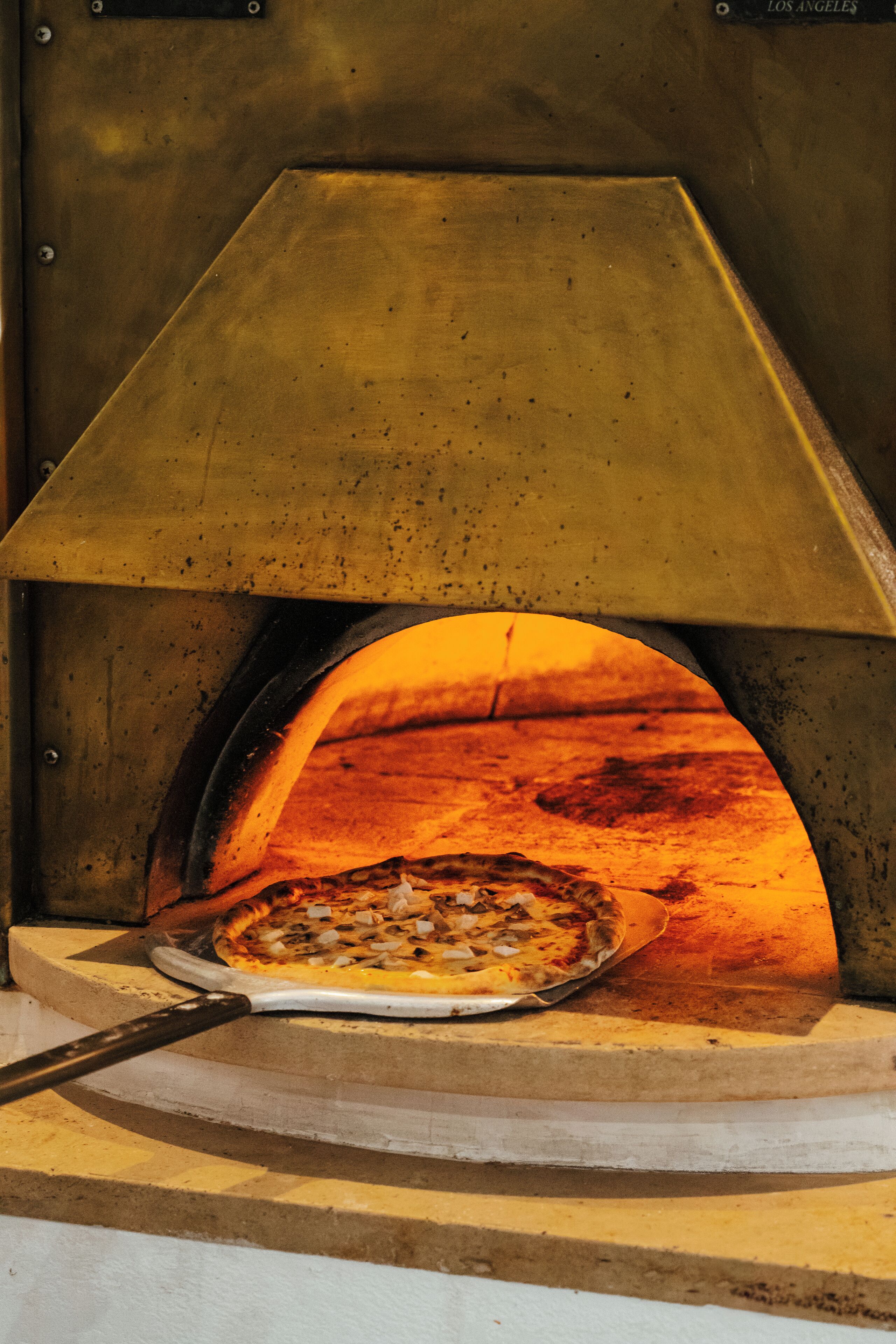 Un horno de pizza con una pizza dentro, una pala para pizza y una estructura de horno de ladrillo.