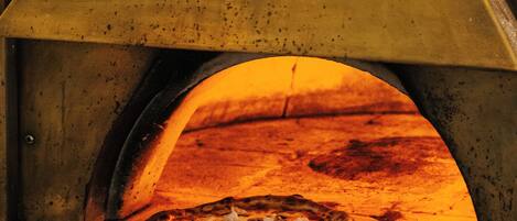 Un horno de pizza con una pizza dentro, una pala para pizza y una estructura de horno de ladrillo.