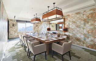 Een moderne eetruimte met een lange tafel, meerdere stoelen, hanglampen en behang met een patroon.
