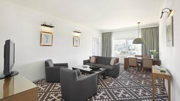 Une chambre d’hôtel moderne comprenant un canapé, des fauteuils, une table basse, un téléviseur, un coin repas et un sol à motifs.