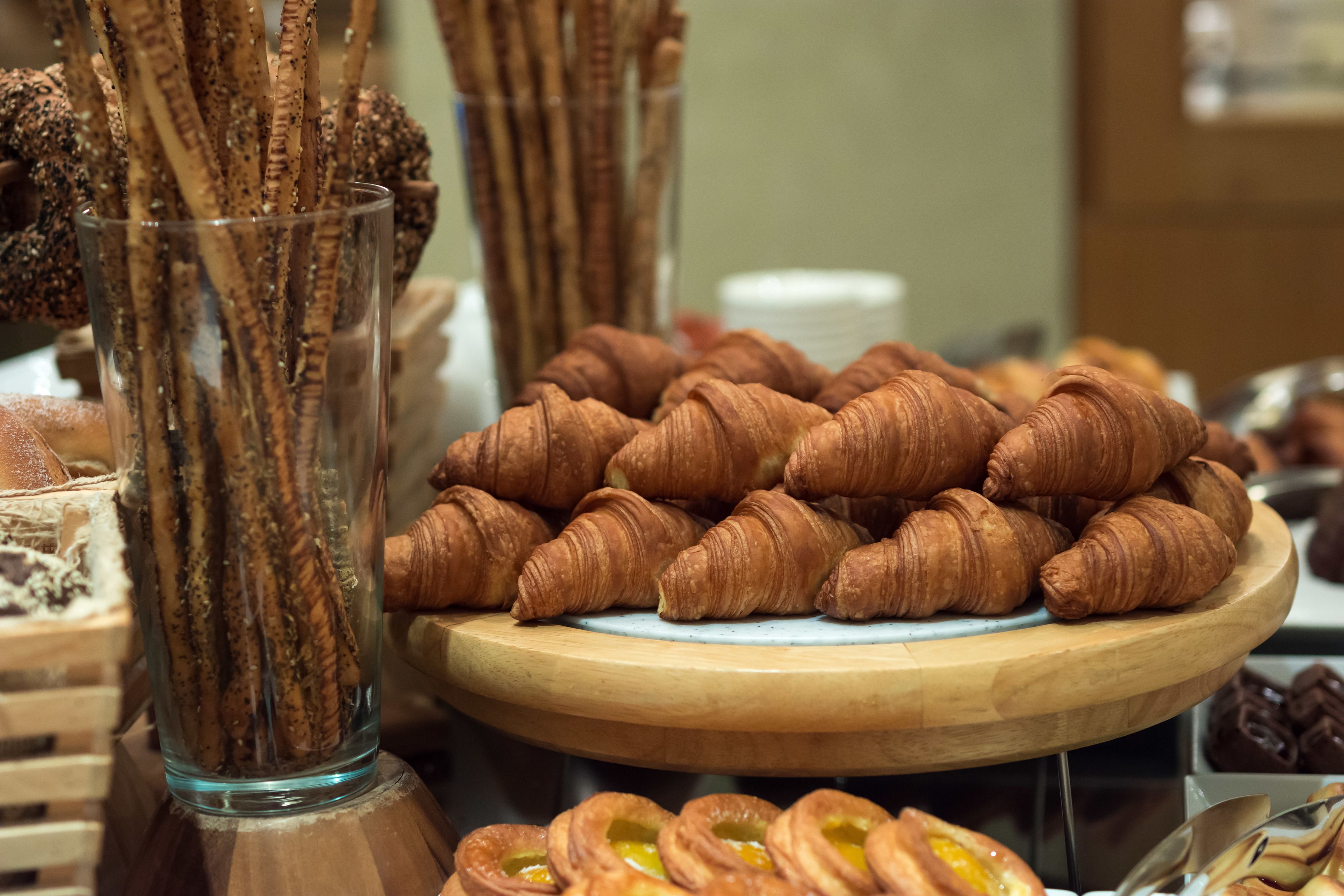 Una exhibición de pasteles, incluyendo cruasanes y otras bollerías, dispuestas sobre una tabla de madera y en un recipiente de vidrio.