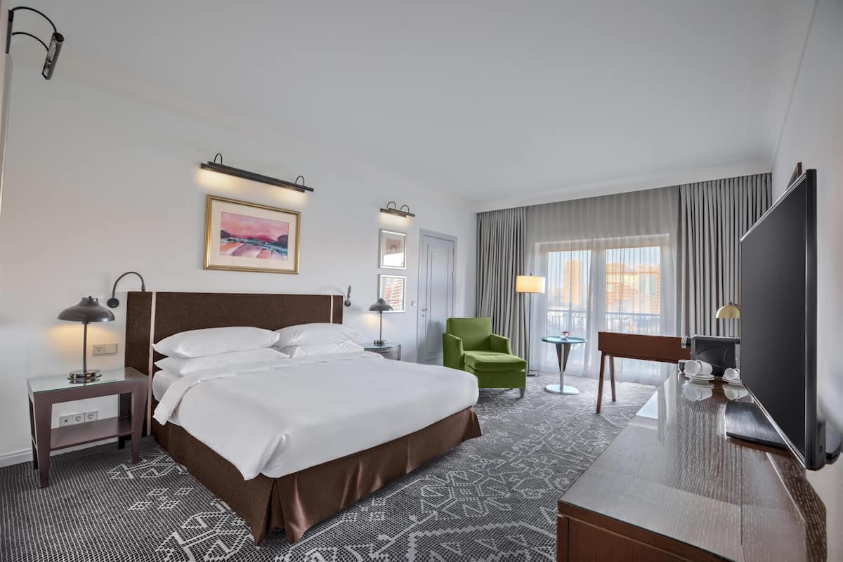 A hotel room with a large bed, a desk, a chair, a TV, and a window with curtains.