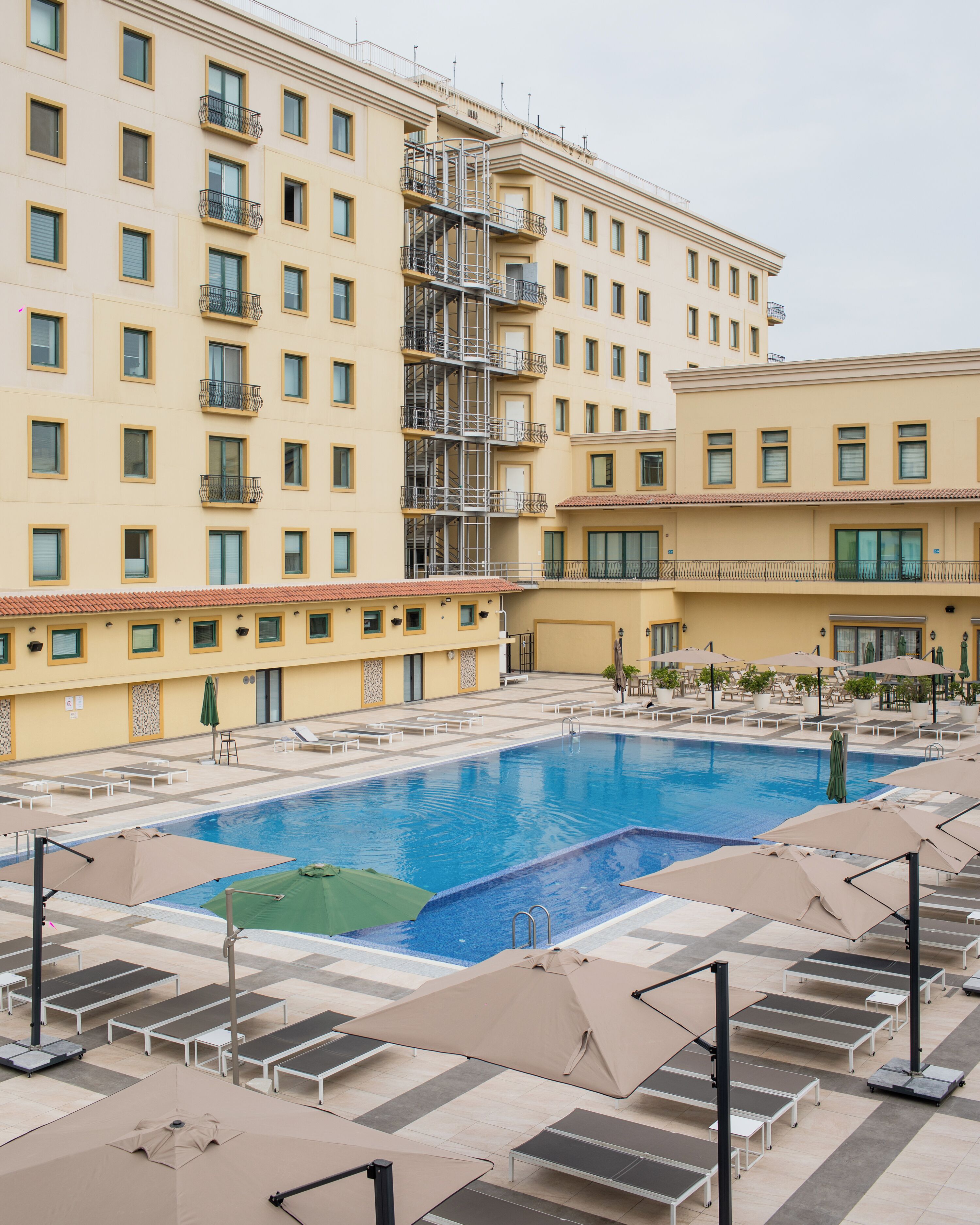 A hotel with a swimming pool, sun loungers, and a covered seating area.