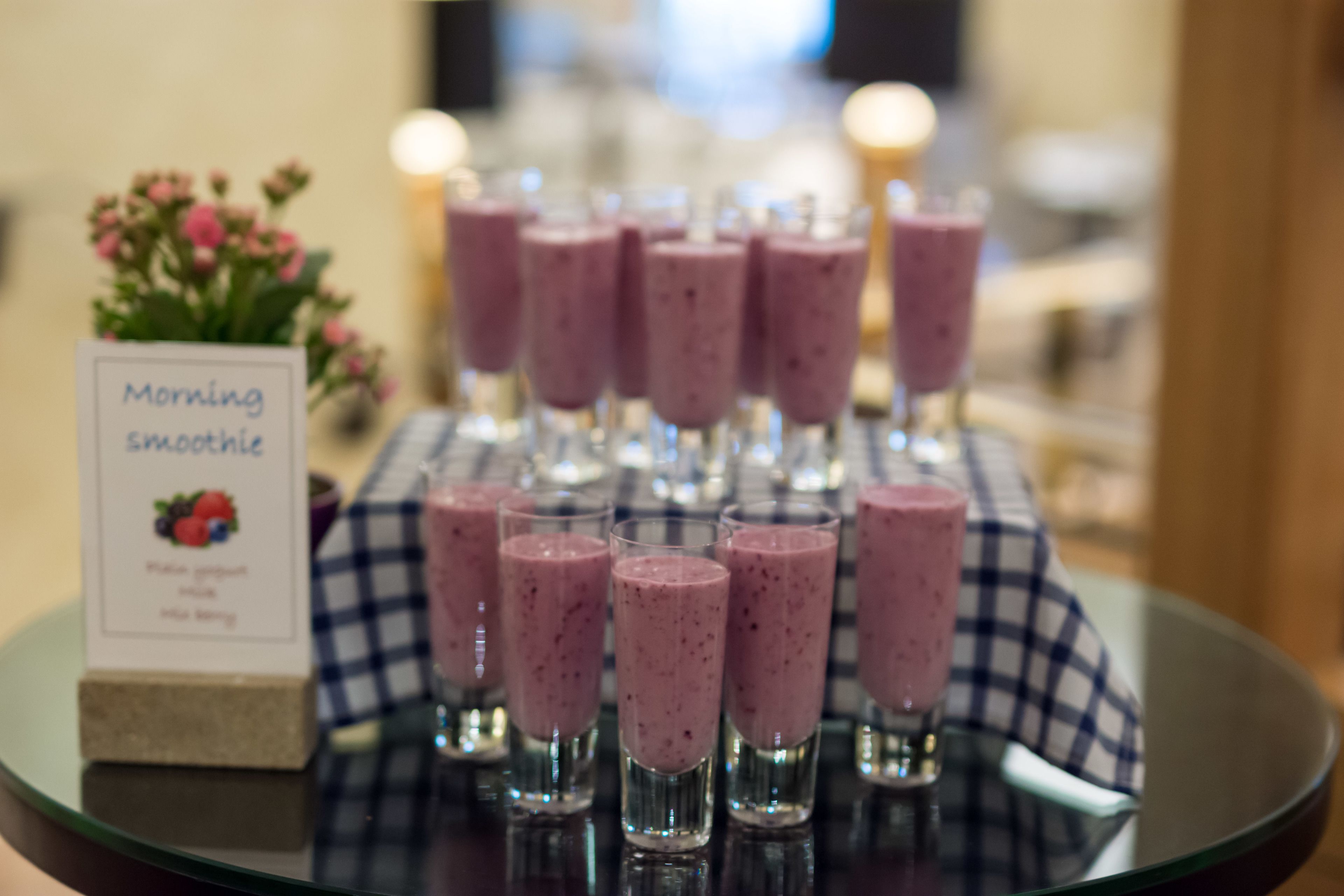 A tray with multiple glasses of pink smoothies on a checkered tablecloth.