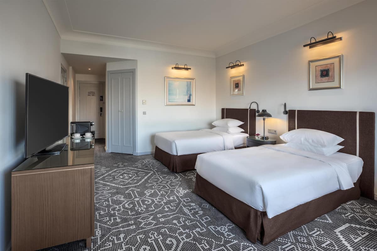 A hotel room with a bed, a desk, a TV, and a patterned carpet.