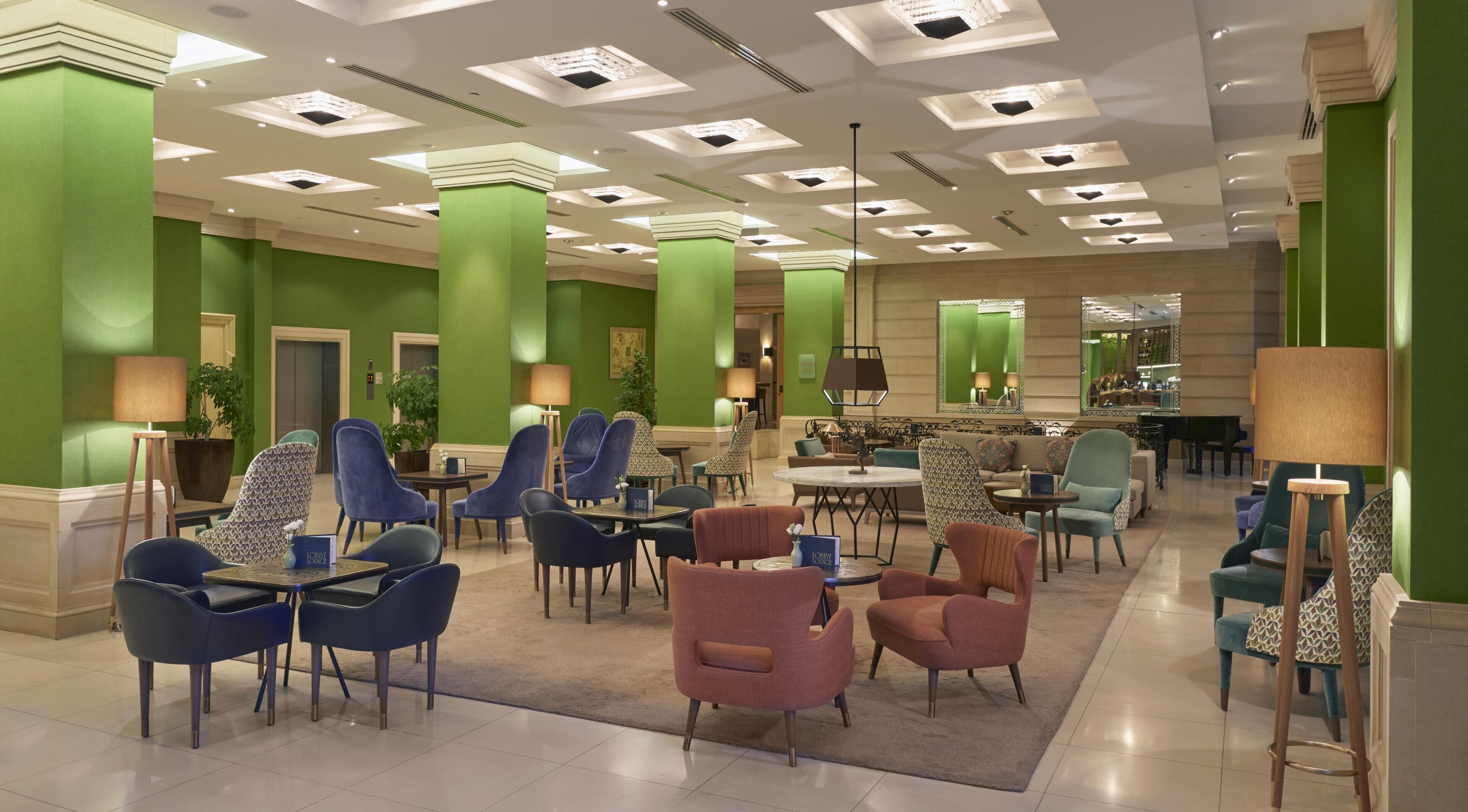 A hotel lobby with green walls, multiple seating areas, and a central coffee table.