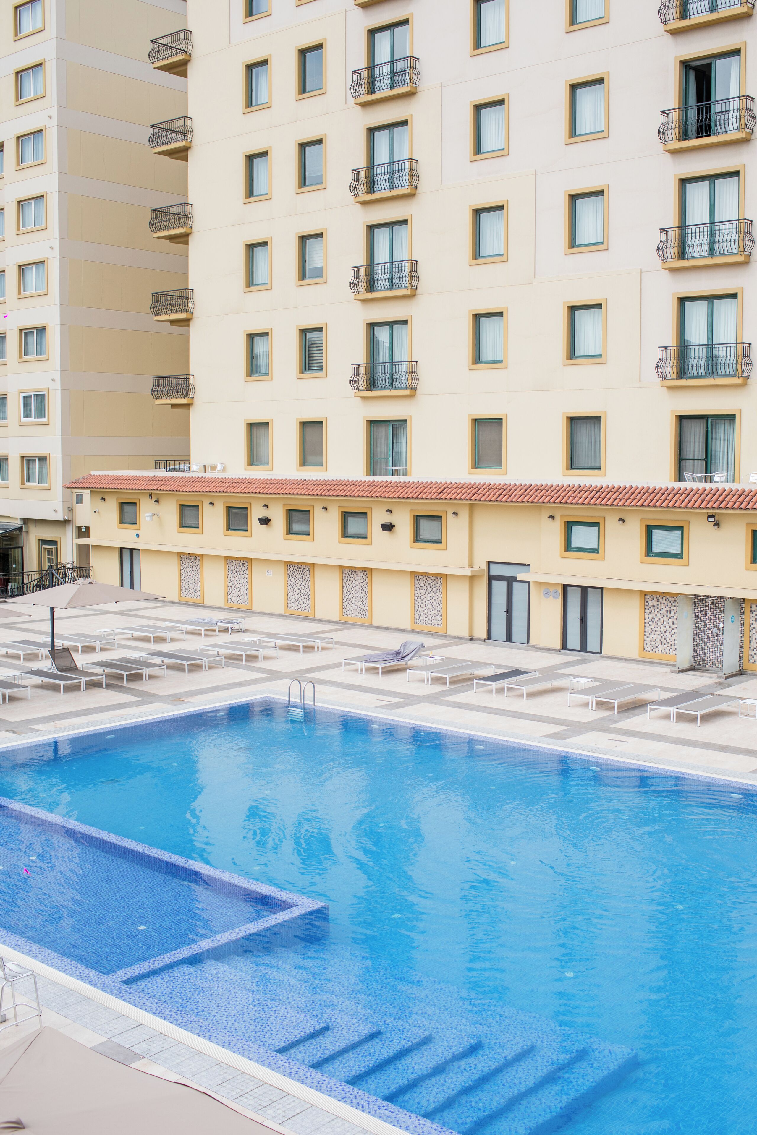 Un hotel con piscina, varios balcones y tejado de baldosas.