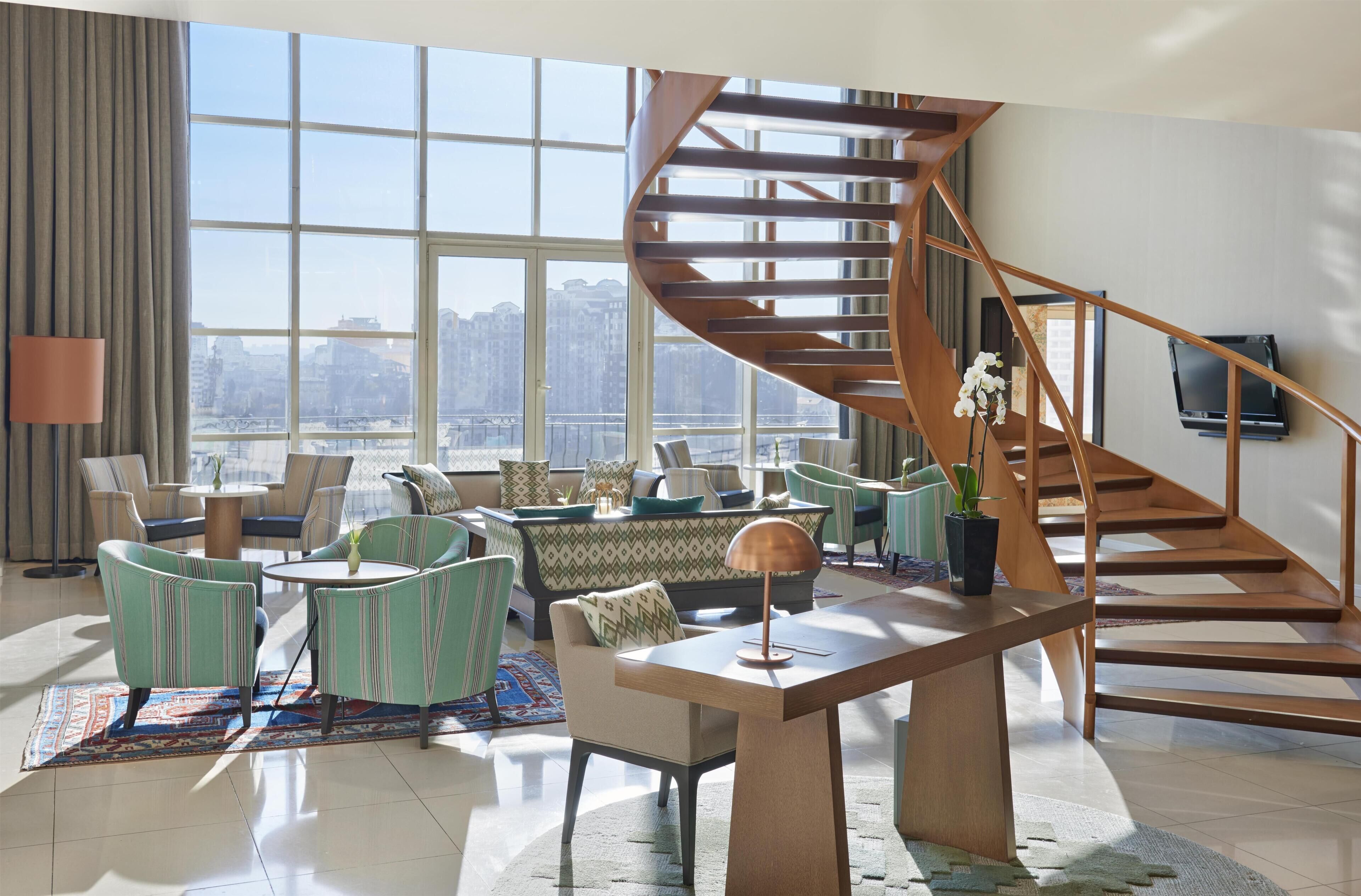 Un salón moderno con una escalera en espiral, ventanas amplias y vistas a la ciudad.