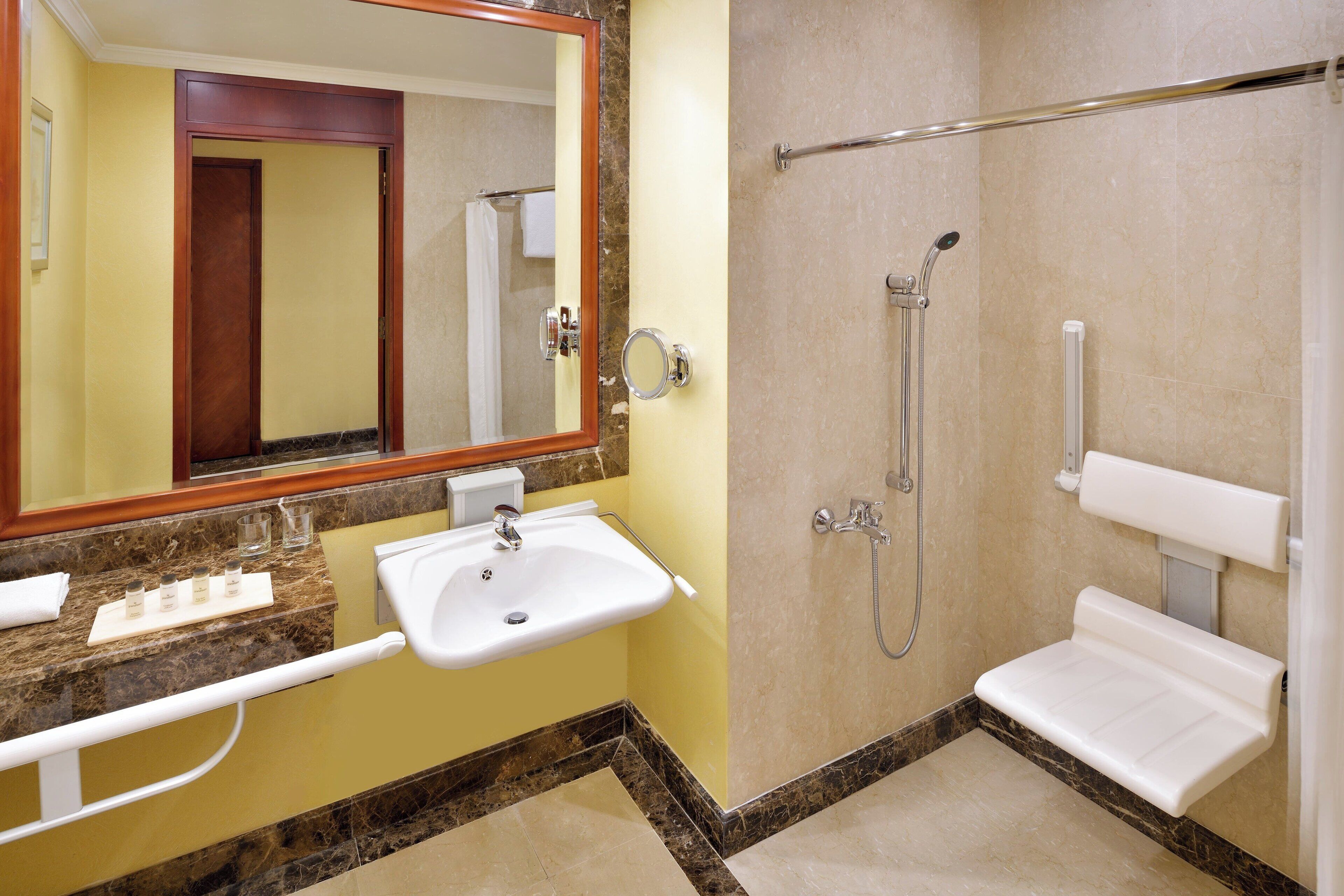 A bathroom with a sink, mirror, shower, and grab bars.