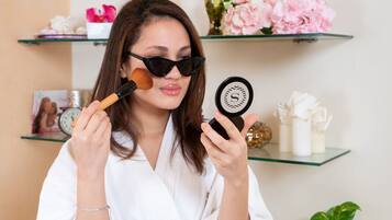 Una persona con bata blanca sosteniendo un espejo de mano y un pincel de maquillaje.