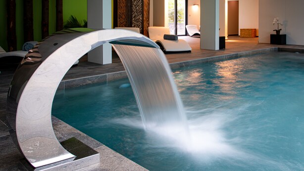 Piscina interna moderna con cascata, circondata da sedie a sdraio e area benessere.