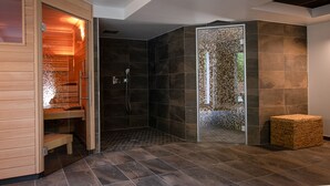 Una moderna stanza spa con una sauna in legno, una doccia a pavimento e un pavimento piastrellato.