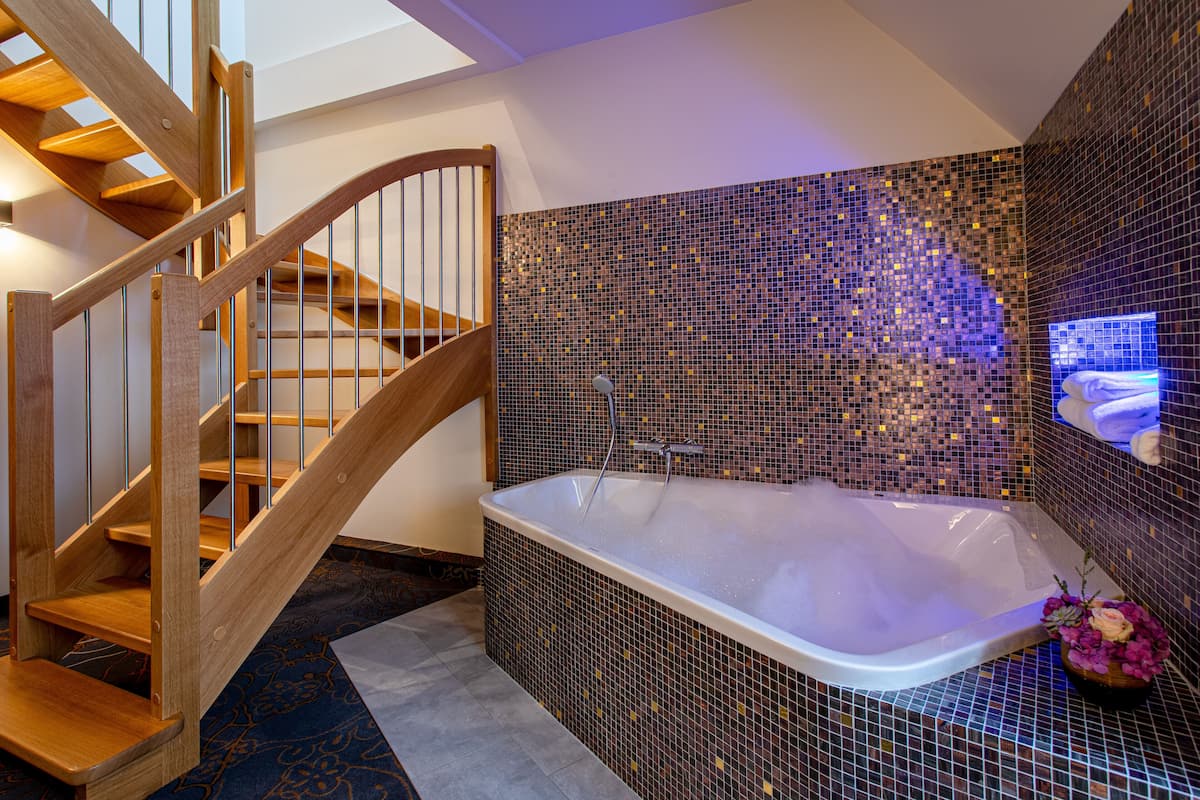 Une salle de bain moderne avec un escalier en bois, une grande baignoire et des murs recouverts de mosaïques.