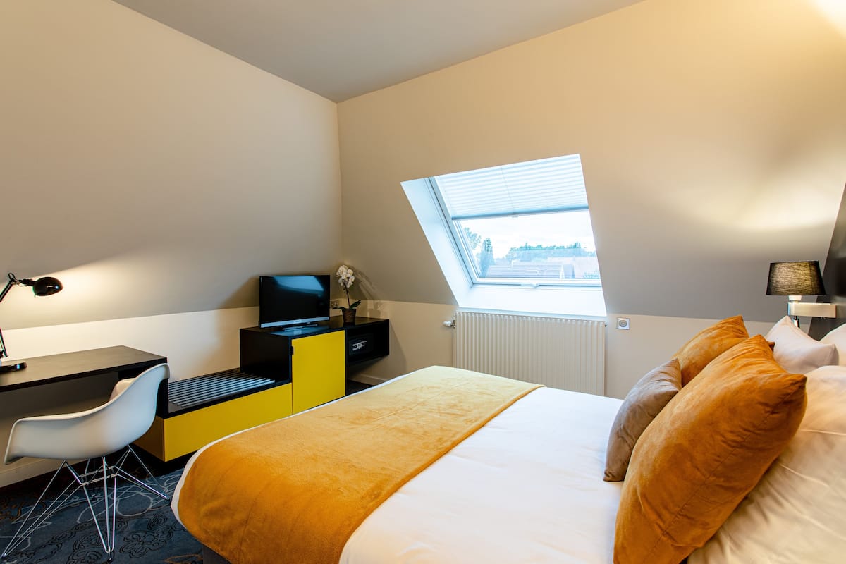 Une chambre d’hôtel équipée d’un lit, d’un bureau, d’une chaise, d’une télévision et d’une fenêtre avec des stores.