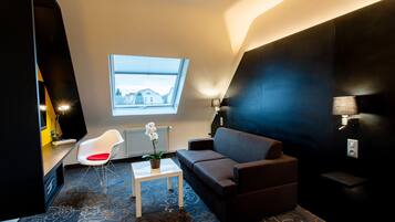 Ein modernes Wohnzimmer mit einer Couch, einem weißen Sessel, einem kleinen Tisch und einem Fenster mit Jalousien.
