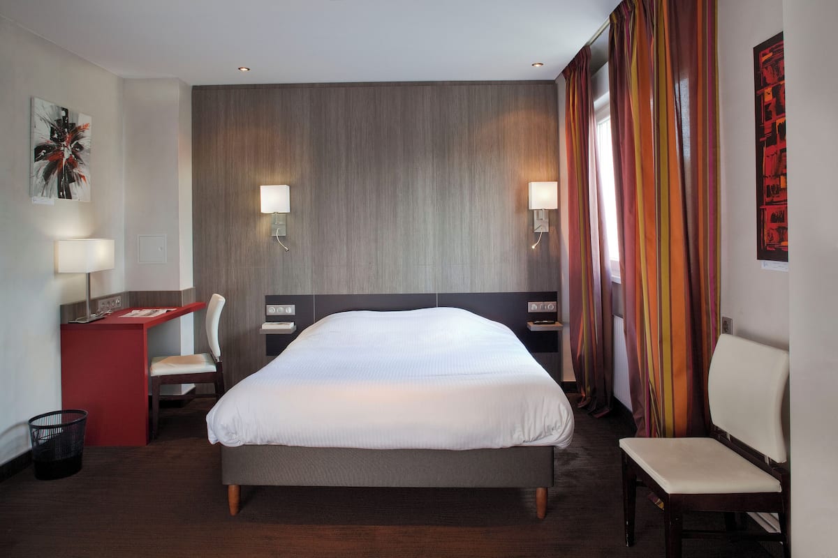 Une chambre d’hôtel avec un grand lit, un bureau avec une chaise, une petite table et un banc.