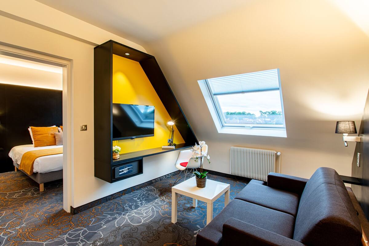 Une chambre d’hôtel moderne équipée d’un lit, d’un canapé, d’une petite table, d’une télévision et d’une fenêtre donnant sur un paysage agréable.