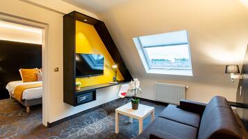 Una habitación de hotel moderna con cama, sofá, una mesita, televisión y ventana con vistas.