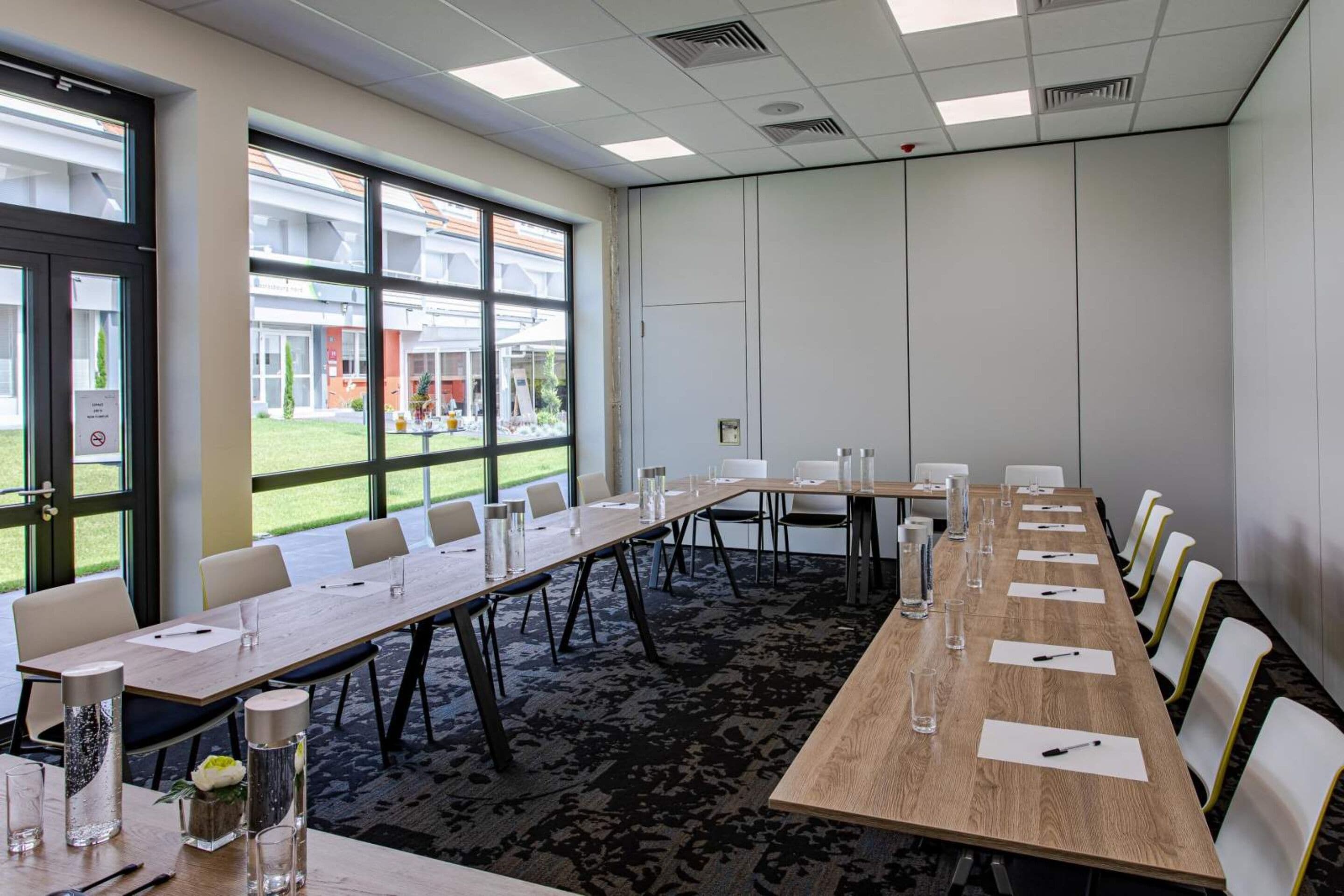 A conference room with a long table, chairs, and a view of a building outside.