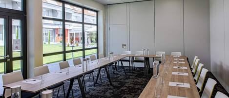 Un salón de conferencias con una larga mesa, sillas y vistas a un edificio.