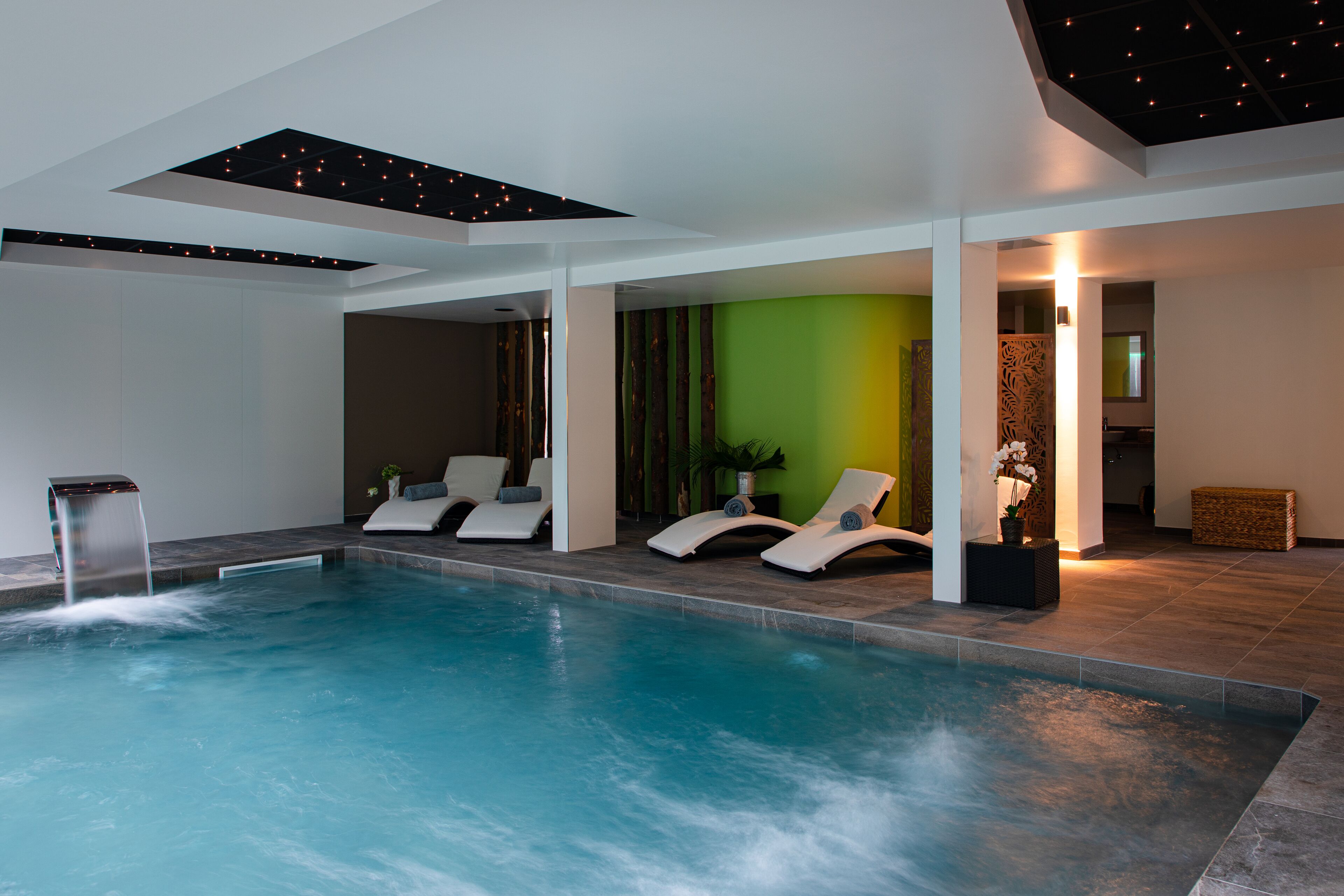 Zona d'una piscina interior moderna amb aigua cristal·lina, gandules i una paret verda decorativa.